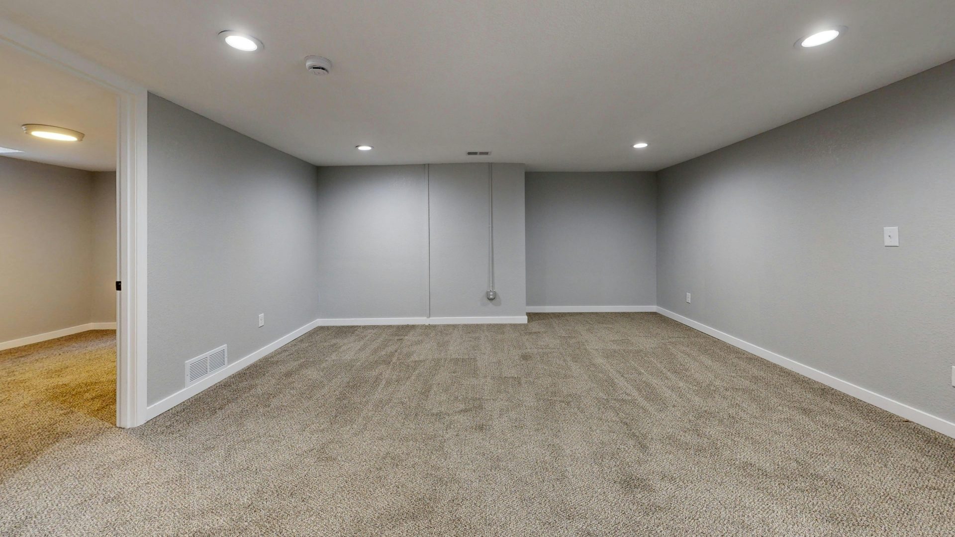 Open basement room with neutral gray walls and plush carpeting, ideal for remodeling.