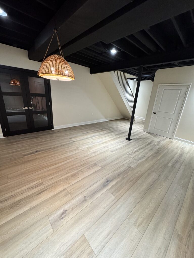Finished basement living area with BRC wall panel system — cream paneled walls, wood-look flooring, black ceiling