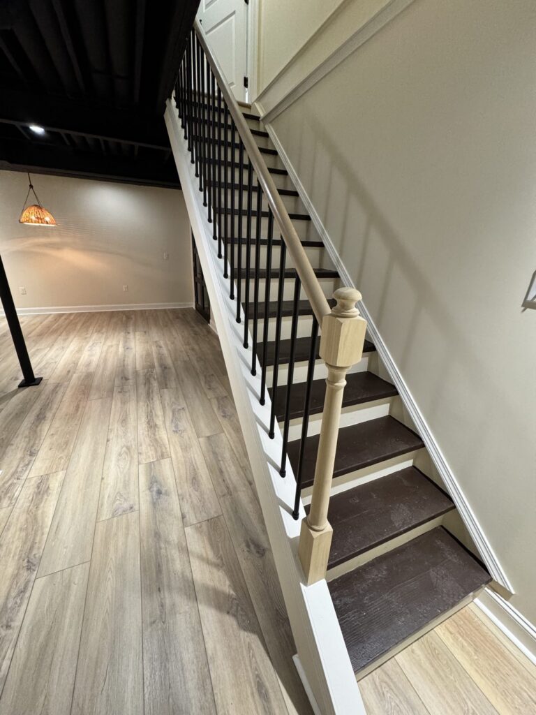 Finished basement staircase with BRC wall panel system — dark wood steps, black railings, cream paneled walls
