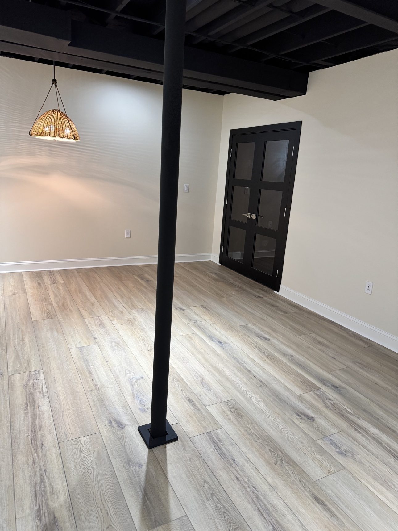 Finished basement living area with wood-look flooring, cream paneled walls, and black support column